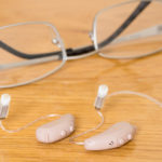 Image: A close-up of a hearing aid next to a pair of glasses